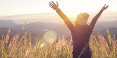 Woman in a wheat field with arms raised high