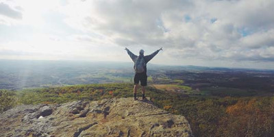 man on mountain top with hands raised in the air
