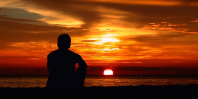 man sitting by the ocean at sunset