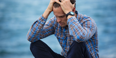 Man by the water with head in hands