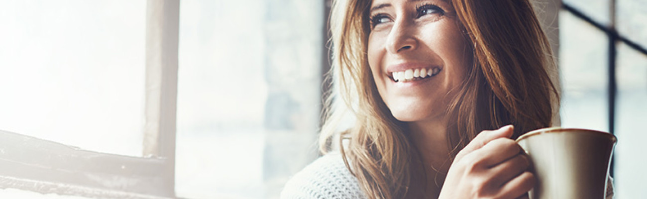 Woman smiling in the sun with a cup of coffee or tea