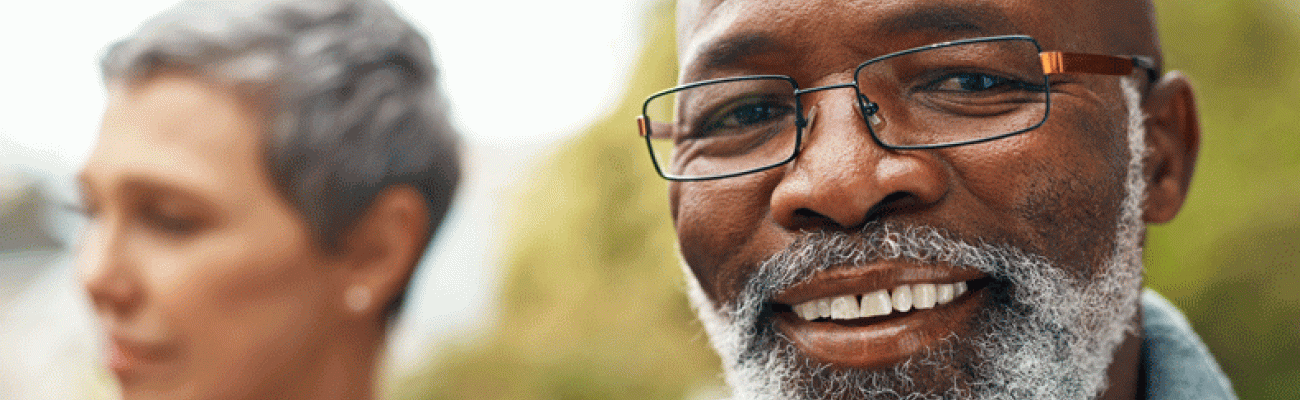 Man smiling at camera with his spouse in the background