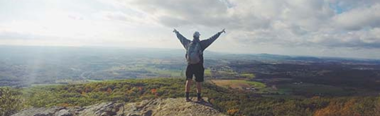 man on mountain top with hands raised in the air
