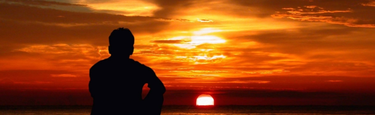 man sitting by the ocean at sunset
